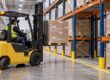 “Loaded forklift approaches a pallet rack bay from a warehouse aisle.”